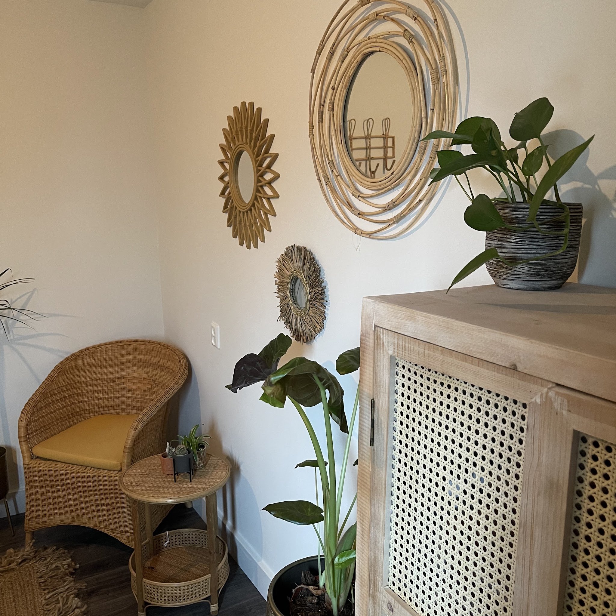 De behandelkamer: rotan spiegels aan de muur, een rieten stoel, planten en een kast met rotan deurtjes