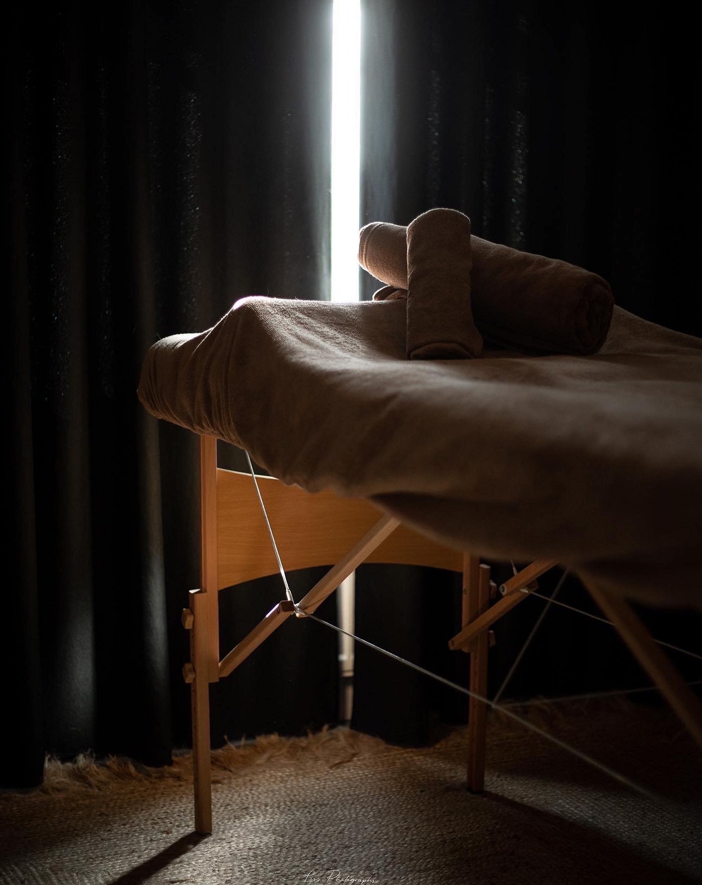 De massagetafel met opgerolde handdoek voor een donker gordijn met een streep daglicht